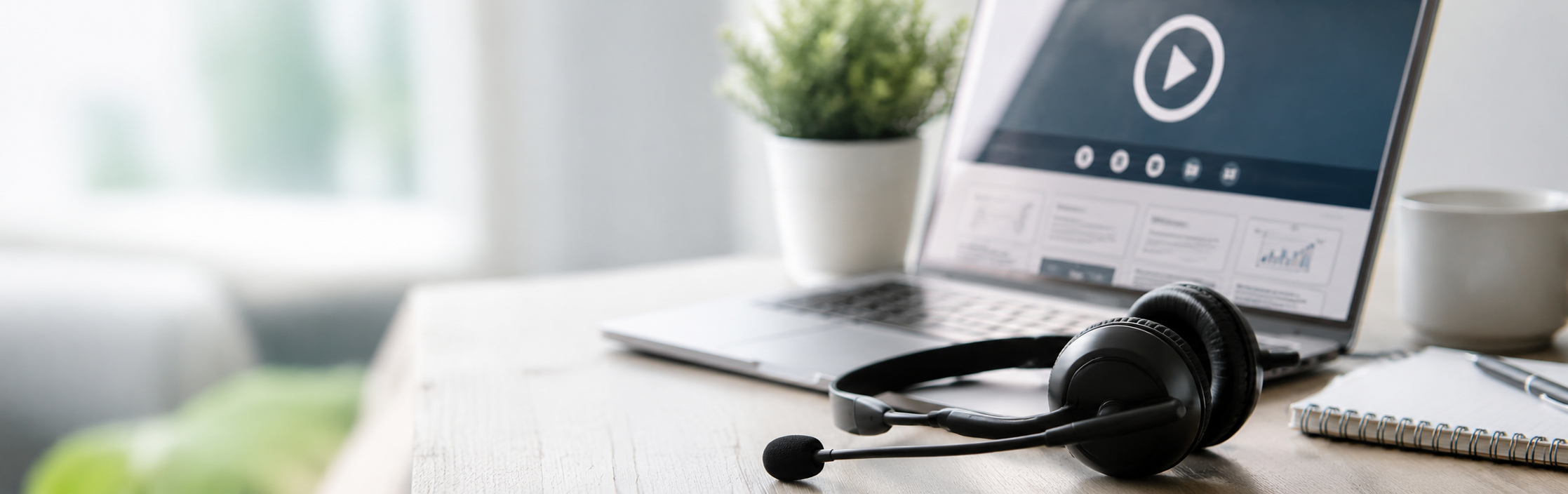 Laptop displaying an online webinar beside a headset and notebook on a desk.